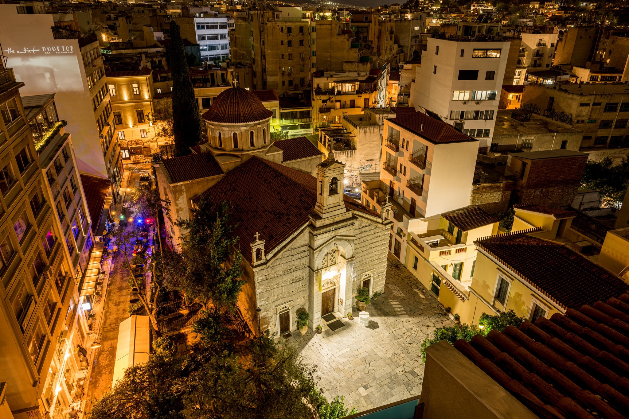 Grecian Nightscape: Illuminated Church Amidst Rooftop Terracotta